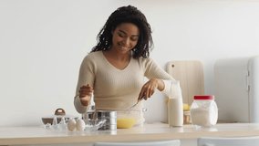 A young African American woman is happily baking in her modern kitchen. She mixes ingredients in a bowl, showcasing her enthusiasm for cooking while preparing a delicious treat. - Powered by Shutterstock - Get 15% off with code: PIKWIZARD15