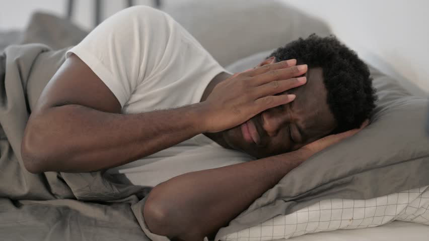 African Man with Headache Lying on Side in Bed