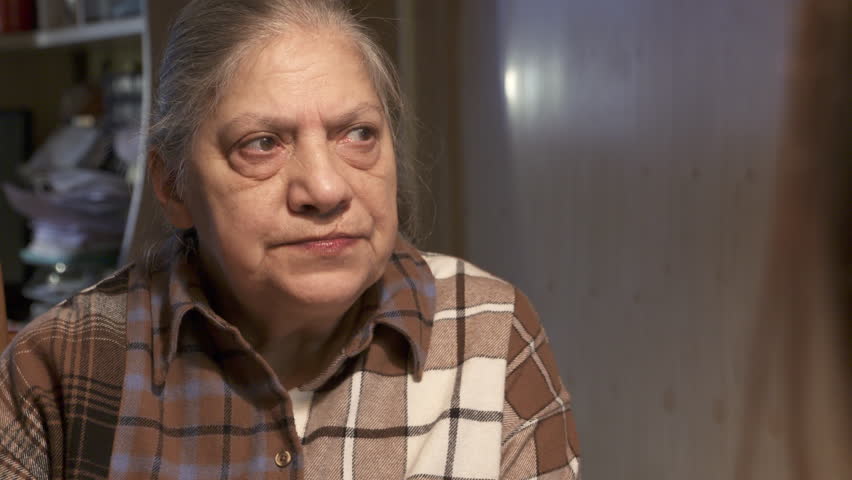 elderly woman, radiating warmth, engages in a heartfelt conversation in her cozy living room, sharing stories that evoke nostalgia and connection with her companion.