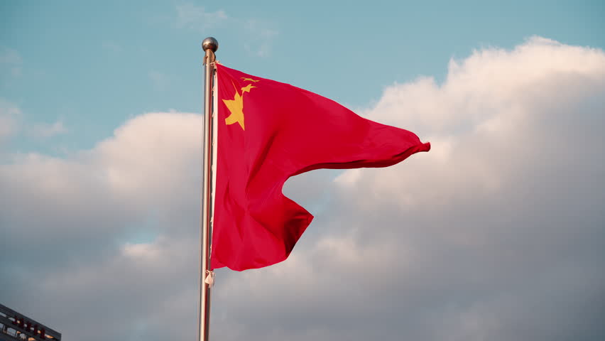 red flag of China flutters against blue cloudy sky.