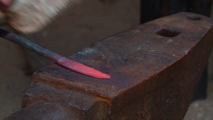 A blacksmith makes a metal blade on an anvil using hammer blows