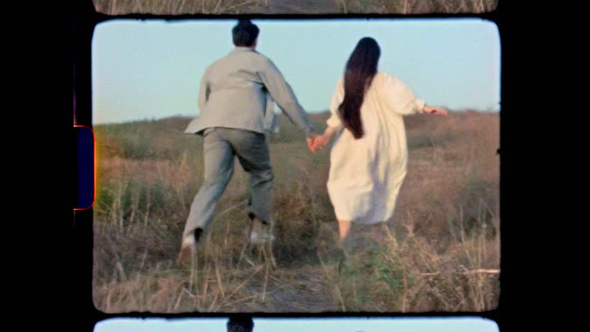 Super 8 footage of young couple running through the hills. Love concept. Free spirit in nature. Beautiful field on the hills. Freedom concept. Uniting with nature