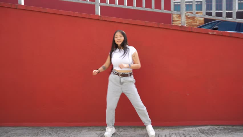 Asian young woman throwing a punch dancing urban dance outdoors against a colorful wall