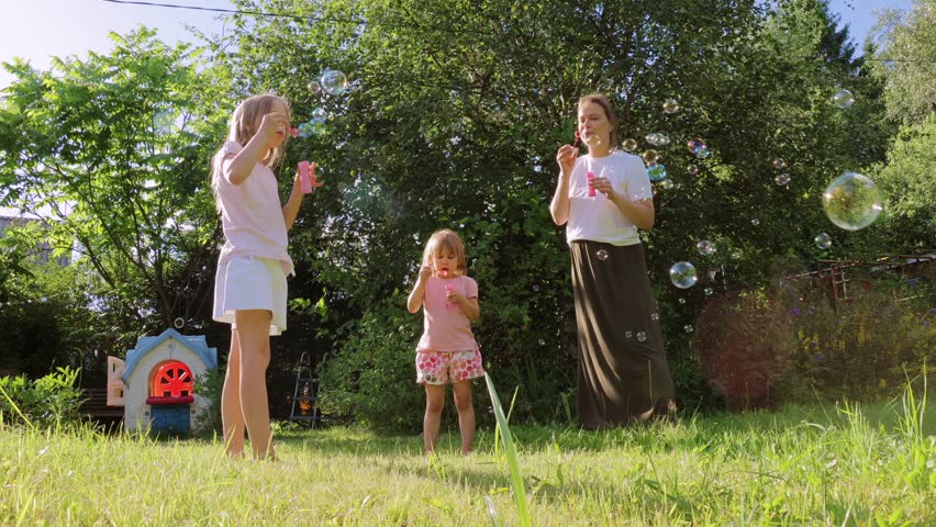 A mother and her two daughters blow soap bubbles together in a sunny backyard, while their playful dog runs around, creating a joyful and carefree family moment surrounded by greenery