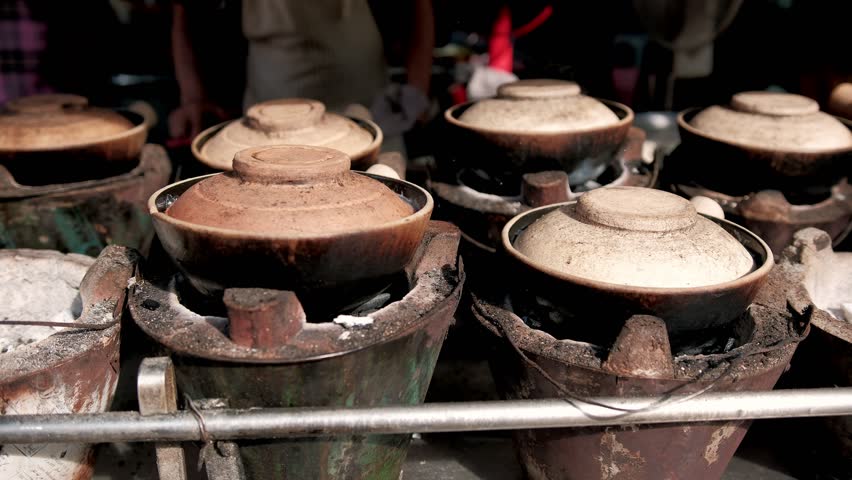 Street food vendor cooking authentic meal in clay pot over charcoal stove, displaying traditional asian culinary culture
