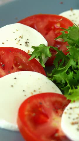 Camera movement of caprese salad with cheese mozzarella tomatoes and fresh salad greens is sprinkled with spices and seasonings. Cooking food. Vertical shot