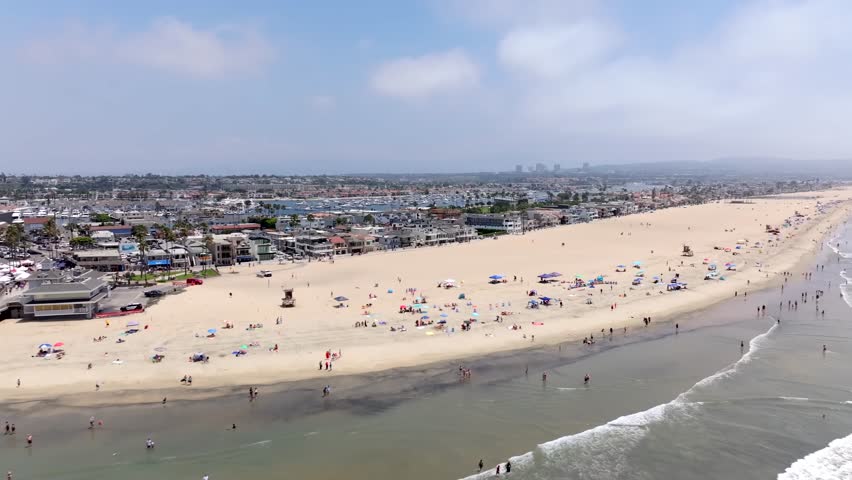 Newport Beach , California on a sunny day with people along the sandy shore - aerial flyover