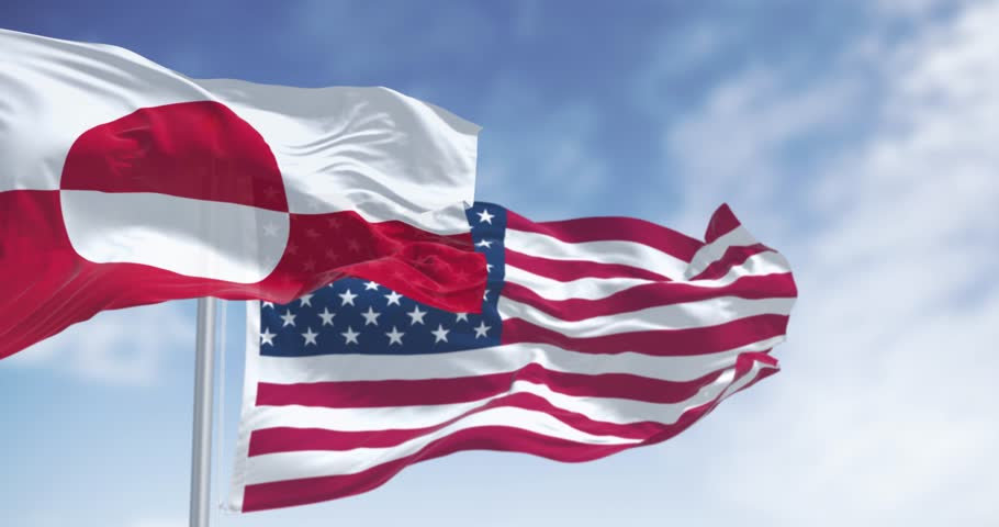 Flags of Greenland and the US waving in the wind on a clear day. Greenland is the world