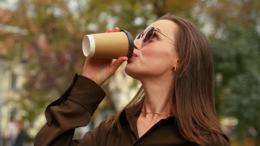 Elegant smiling Caucasian woman businesswoman girl female business lady in dark sunglasses walking in city walk outdoor go fashion style going street outdoors drinking holding cup coffee drink enjoy