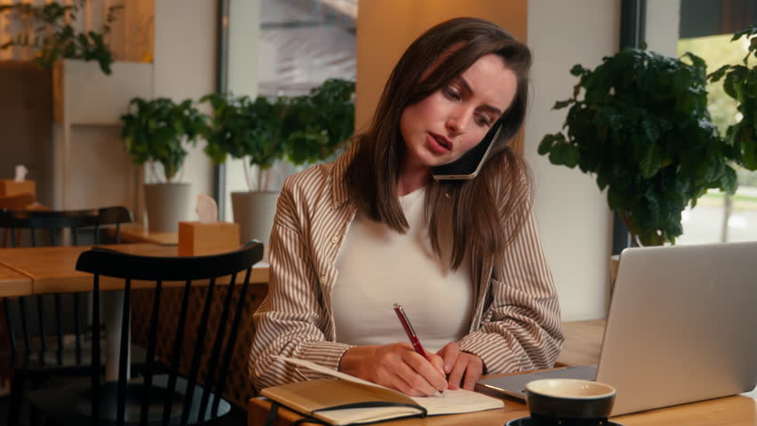Caucasian busy multitasking woman businesswoman female business girl talking mobile phone call conversation communicate writing notes information typing laptop online internet computer work in cafe - Powered by Shutterstock - Get 15% off with code: PIKWIZARD15