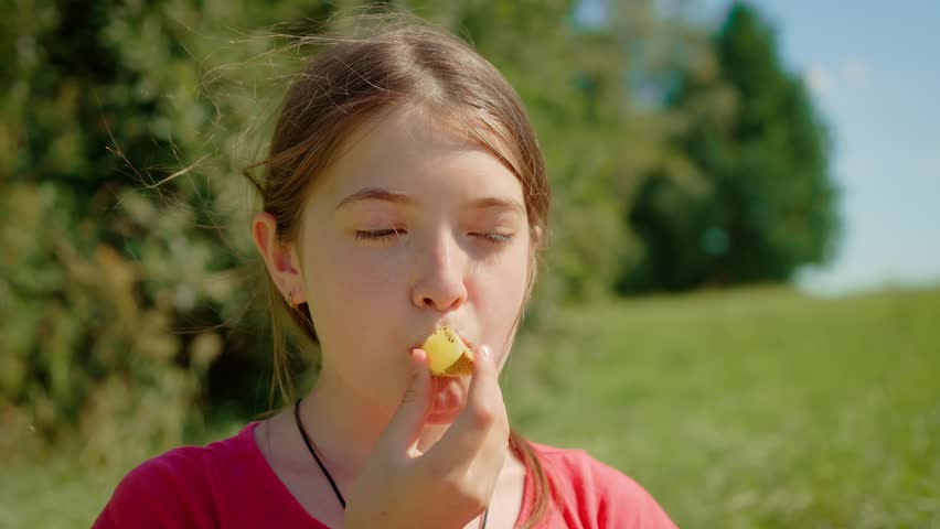 Young girl eating yellow kiwi, biting into soft fruit. Kid enjoying sweet yellow kiwi outdoors, savoring unique flavor. Child tasting fresh yellow kiwi, appreciating smooth texture in sunny