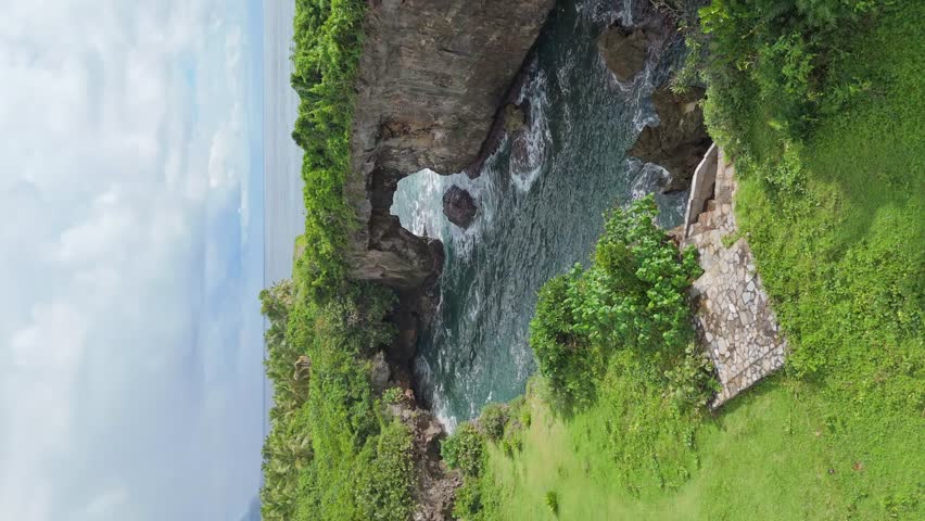 Vertical static view of La Hondonada natural rock arch with waves and lush greenery in Las Galeras, Samana, Dominican Republic
