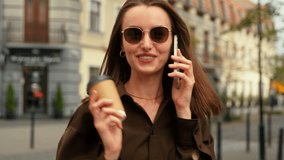 Elegant smiling Caucasian woman businesswoman girl female business lady in dark sunglasses walking in city walk outdoor go fashion style talking mobile phone call smartphone discuss holding cup coffee - Powered by Shutterstock - Get 15% off with code: PIKWIZARD15