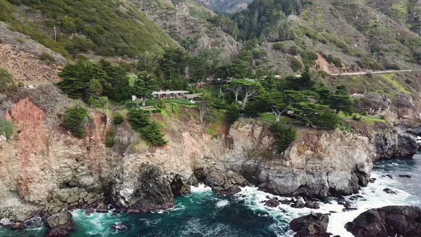 Aerial shot on Mansions in Northern California on top of a cliff with waves crashing from the Pacific Ocean. Big Sur, California