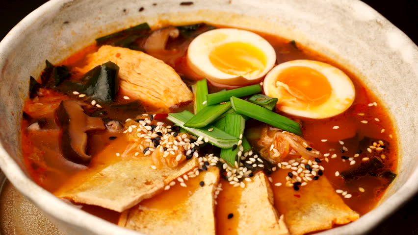 Japanese Ramen with beef or chicken, rice noodles with fried meat, Tom Yum rotates on the right background, close-up, vertical video. Spicy Thai Asian soup, chef cooks in traditional Korean Chinese cu