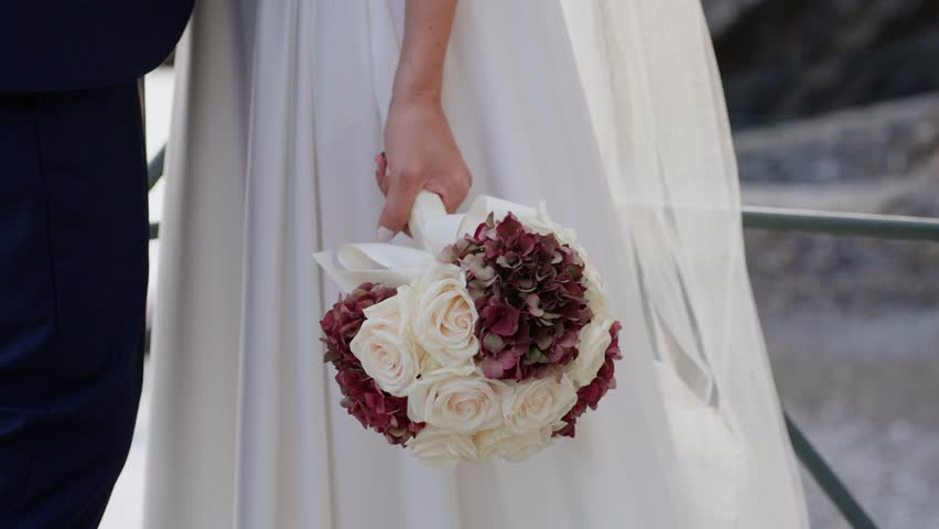 A bride holding a bouquet of roses and hydrangeas near the sea in Liguria, Italy