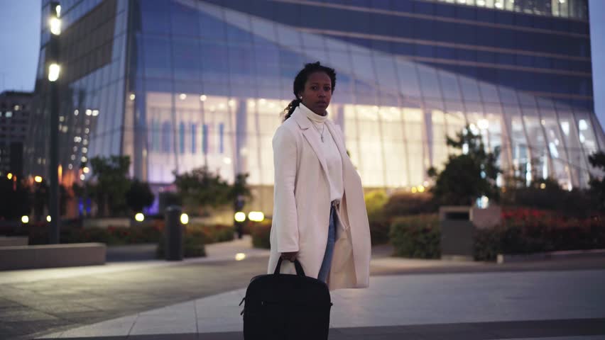 African American business woman checking the time, and walking out of financial district after work holding a suitcase. 