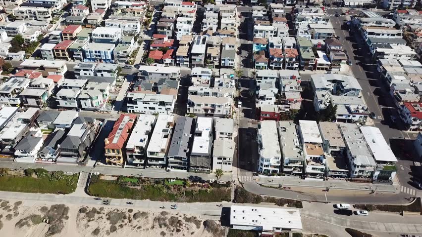 Cyclist on beach Promenade of Manhattan Beach in Los Angeles. Sunny day in summer season. Luxury homes and apartments in first row. Aerial descend shot.