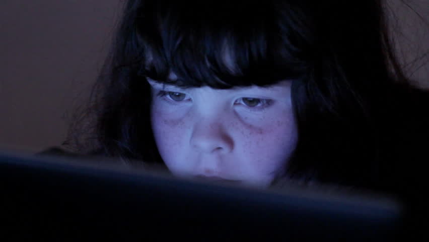 Child's face lit by computer screen in dark room
