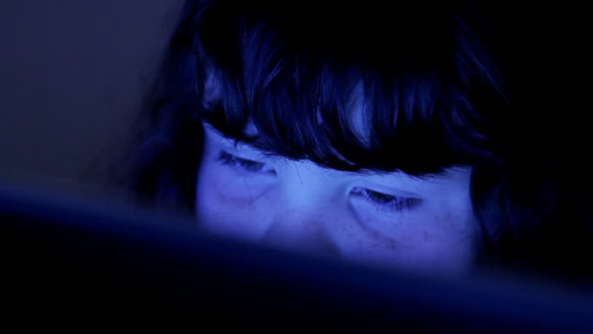 Child's face lit by computer screen in dark room, CU