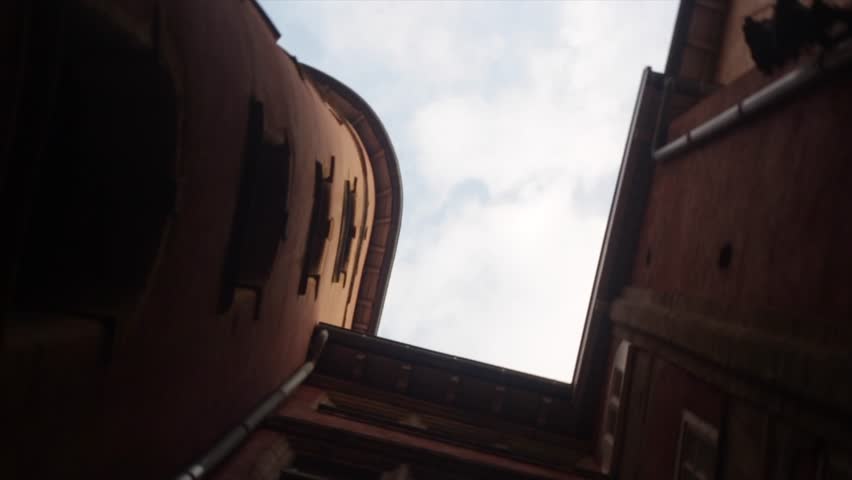 Low-angle view revealing hidden passage between historic buildings, clouded sky peeking through narrow pathway