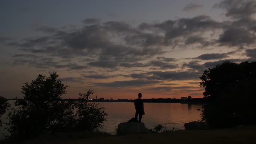 The shadow of a man is contemplating and looking into the lake at sunset. Lake Ontario, Canada.