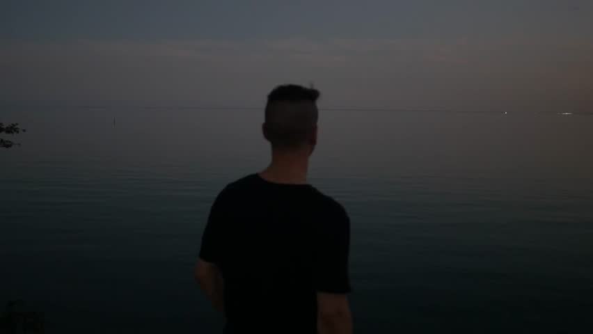 The shadow of a man is contemplating and looking into the lake at sunset. Lake Ontario, Canada.