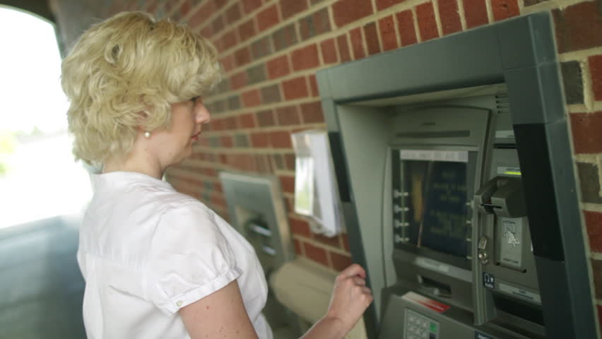 Woman using an ATM, turns to the camera and smiles at end of clip. Canted camera