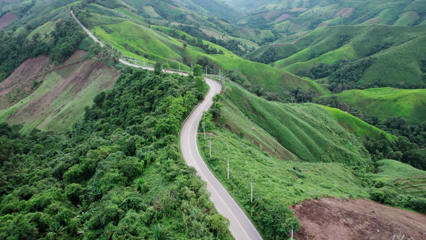 Aerial view of country road in forest. Cinematic drone shot flying over country road with curved in the mountain. 