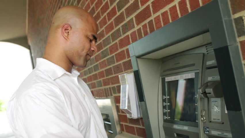 Man using an ATM, turns to the camera and smiles at end of clip. Canted camera