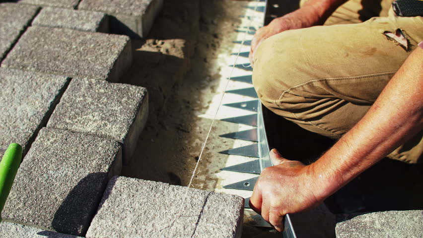 Worker aligning paving bricks for pathway construction