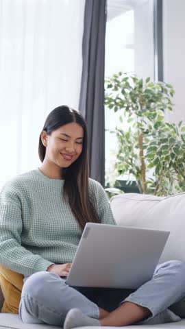 Video of cute woman working with laptop sitting on the couch at home.