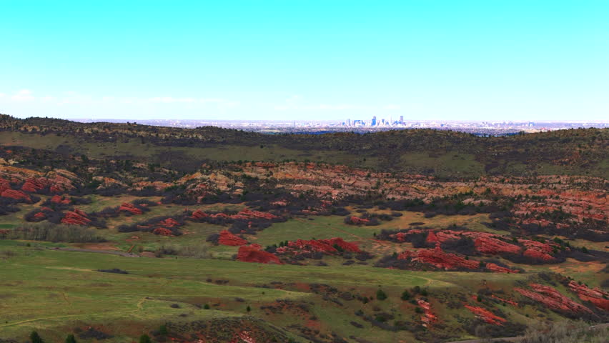 A drone view of colorful hilly landscape under clear sky in downtown Denver, Colorado in the distance from Ken Caryl Valley