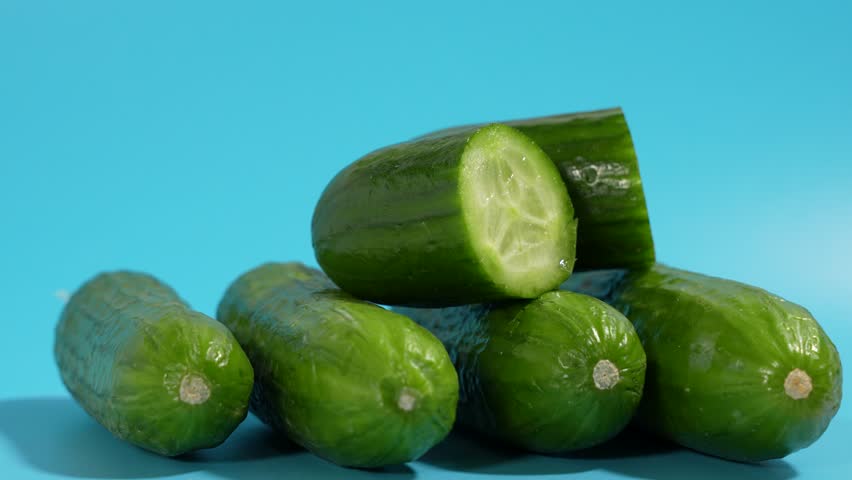 A pile of cucumbers rotates on a blue surface. One of the cucumbers has been cut in half