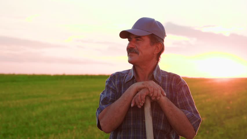 glad Latin American farmer with cap looking away and returns facing at the camera cheerfully and smiling at sundown. Portrait of the successful senior farmer with moustached smiling at camera