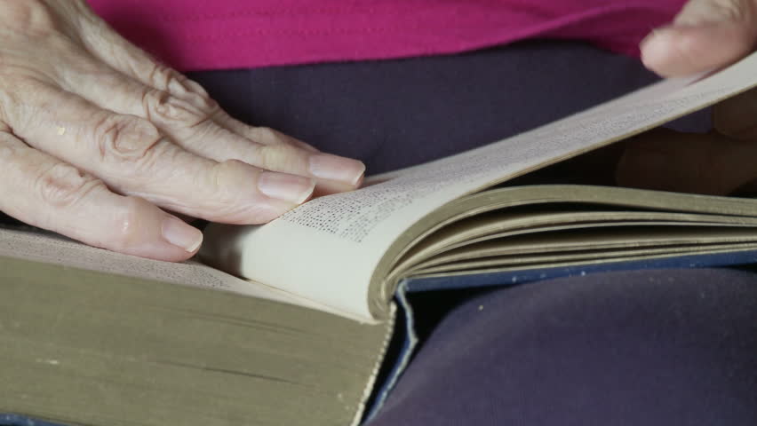 Elderly woman's hands, deformed by arthritis, turn the pages of an old book.