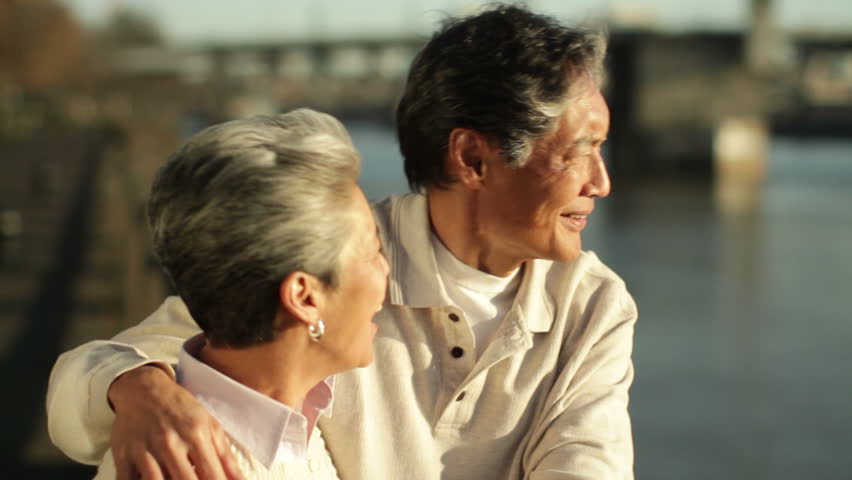 Older Asian-American couple standing, talking and looking out at the Willamette