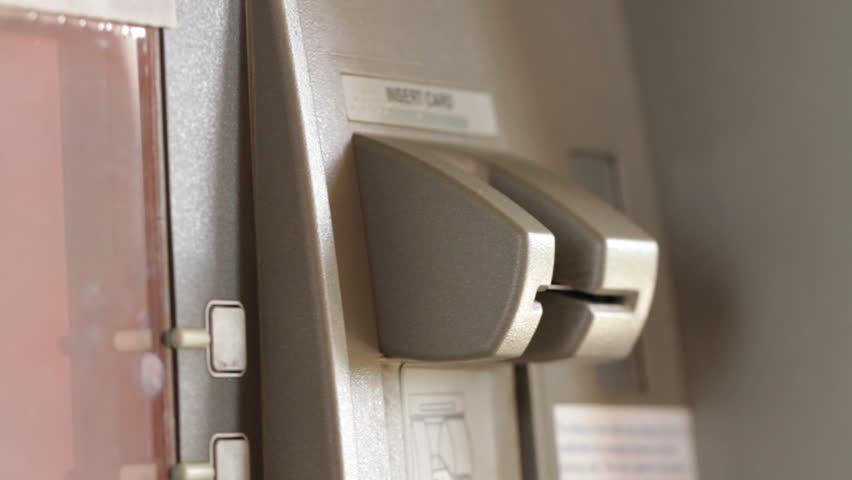 Detail of a woman's hand inserting and removing a bank card at an ATM.