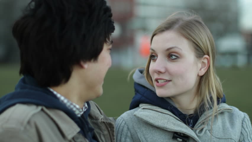 Good looking young man and woman talk and laugh while sitting on a park bench.