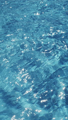 Ripples on the water of the pool, transparent, sparkling, inviting surface of the water in motion, view from above. slow motion and looped vertical video.