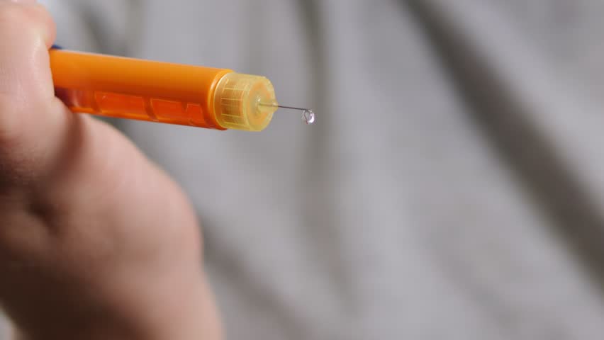Close-up of a woman holding an insulin syringe pen, insulin is dripping from the needle The medicine drips from the syringe. Diabetes treatment.