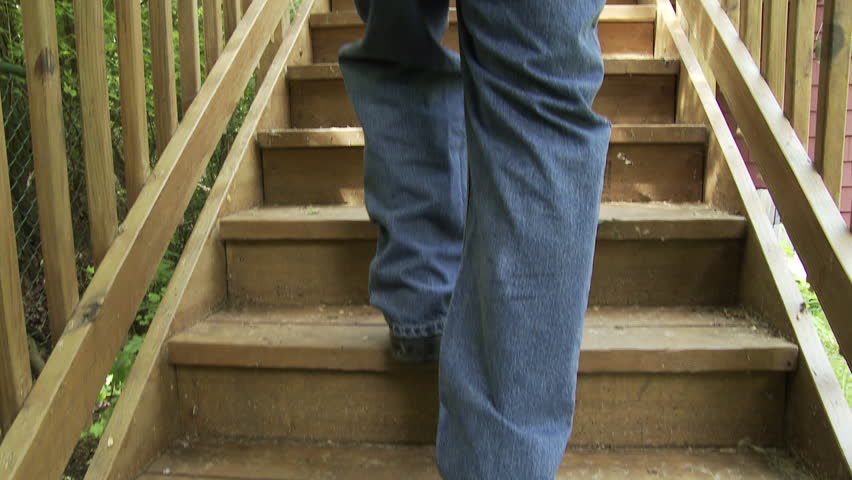 Man's legs and feet, blue jeans, black shoes, walk up a wooden staircase. Jib