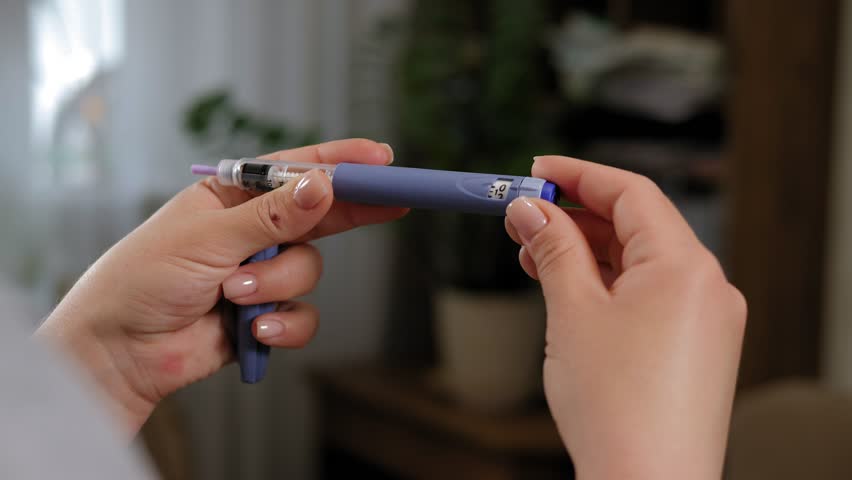 Close-up of an unrecognizable diabetic woman dialing the correct dose of insulin on a syringe pen before an injection. The concept of medicine and treatment of type 1 diabetes.