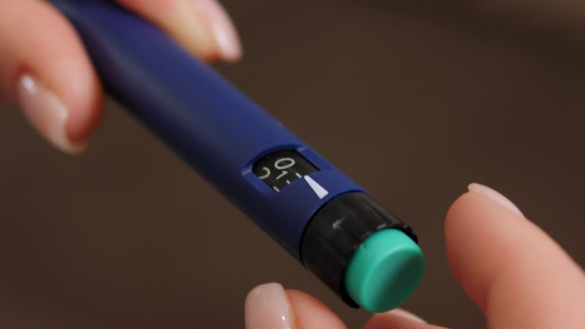 Close-up of a woman holding an insulin syringe pen in her hands, she is gaining the required dose of prolonged or short insulin before the injection. 