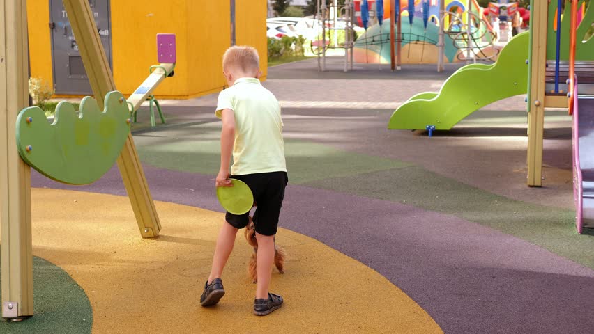 A little boy is playing with a frisbee dog in the yard of the house on the playground. A Yorkshire terrier plays with a plate in a modern courtyard of a residential complex.