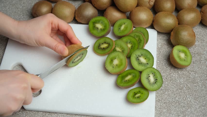 The process of cutting fresh ripe kiwi into slices with a knife.