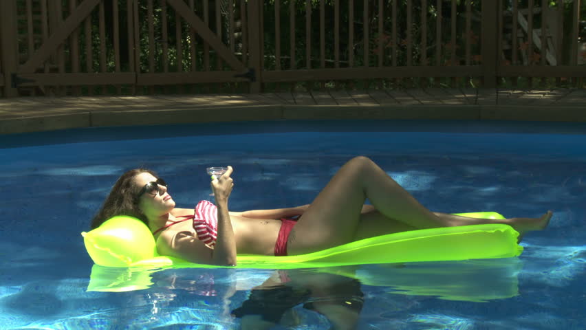 Beautiful woman floats with her cocktail on a swimming pool, then she's thrown