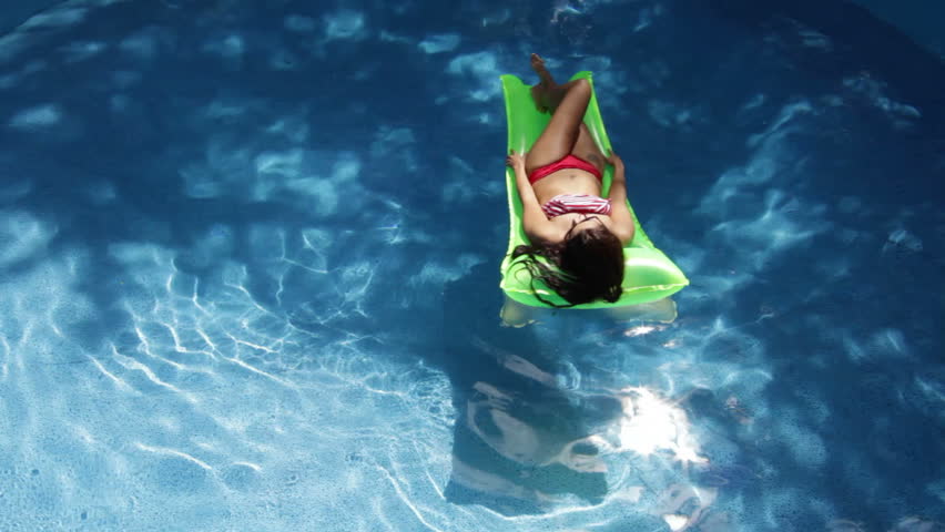 Beautiful woman sunbathing on a floating mattress on a sparkling swimming pool.