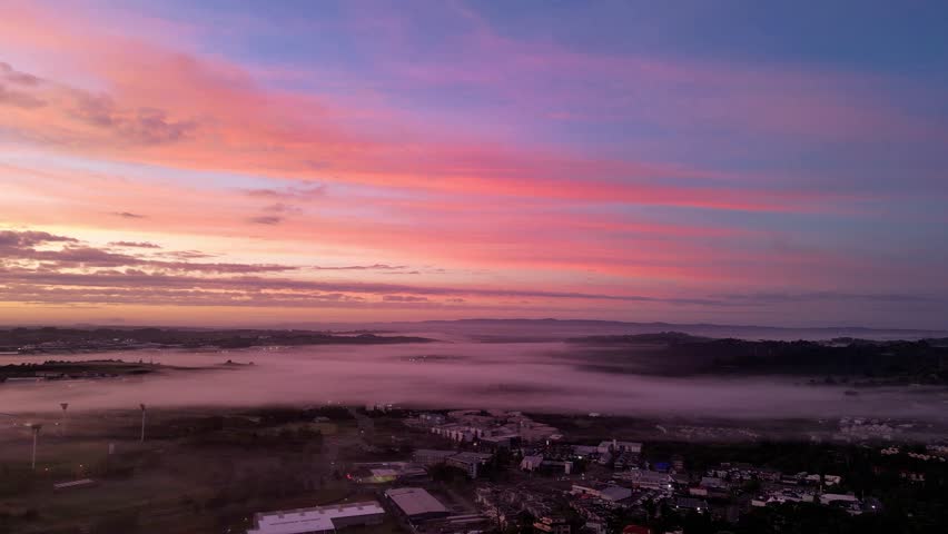 An aerial footage of the city of Auckland covered with fog at sunrise, with scenic dawn sky in the background, New Zealand