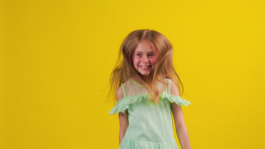 Happy kid girl in the blue dress jumping in studio. cute children dancing and jumping raising hands up. studio shot, yellow background